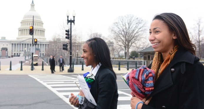Two women in black coats walking across the street from the U.S. Congress building.