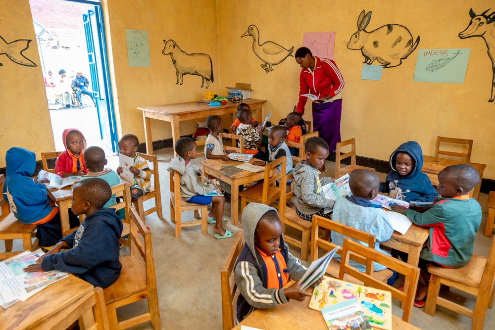 Children sitting around tables and an adult in a room.