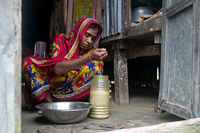 Rina Begum stores rice in a watertight container. This will ensure her family has food to eat when the next cyclone hits. Photo by Jennifer Hardy/CRS