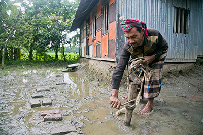 Almas Sikdar Almas ties a secure rope to a roof brace of his house, which will reduce flying debris and damage to the home in future cyclones. Photo by Jennifer Hardy/CRS