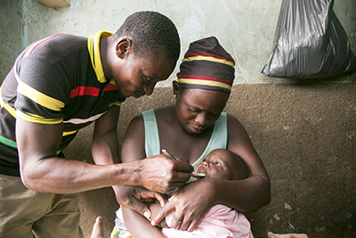 Amour Collette's son, Adam Barnabas, receives free malaria medication from Simon Aiyana, a community health worker trained by CRS in Benin. Photo by Michael Stulman/CRS