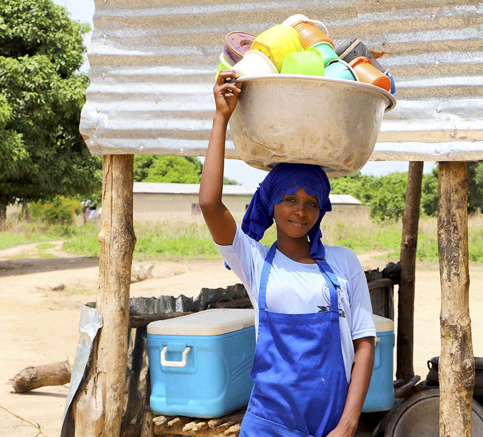 Benin school cook holding large pan on head