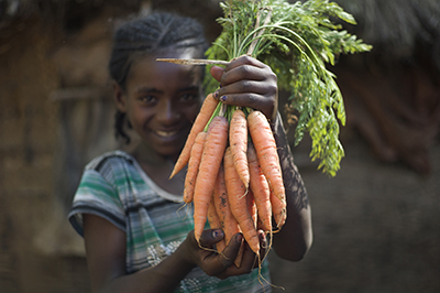 Biranesh Getu, 9, poses with a batch of freshly picked carrots. Photo by Ric Francis for CRS