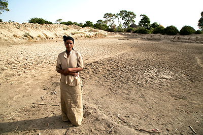 Badoo Fukura stands at the bottom of a basin that used to be the community watering hole. It served about 30 different families before going dry in October. Photo by Nancy McNally/CRS