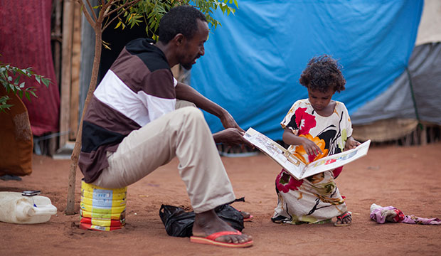 Ahmed Hussein and his daughter study a book on hygiene and sanitation outside their shelter at the Kambioos refugee camp in Kenya, where they sought refuge from the famine in Somalia. Photo by Sara A. Fajardo/CRS