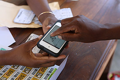 A farmer in Madagascar signs her name on the touch screen of an iPod before receiving barcoded vouchers that she'll use to purchase seeds for planting. Photo by Sara A. Fajardo/CRS