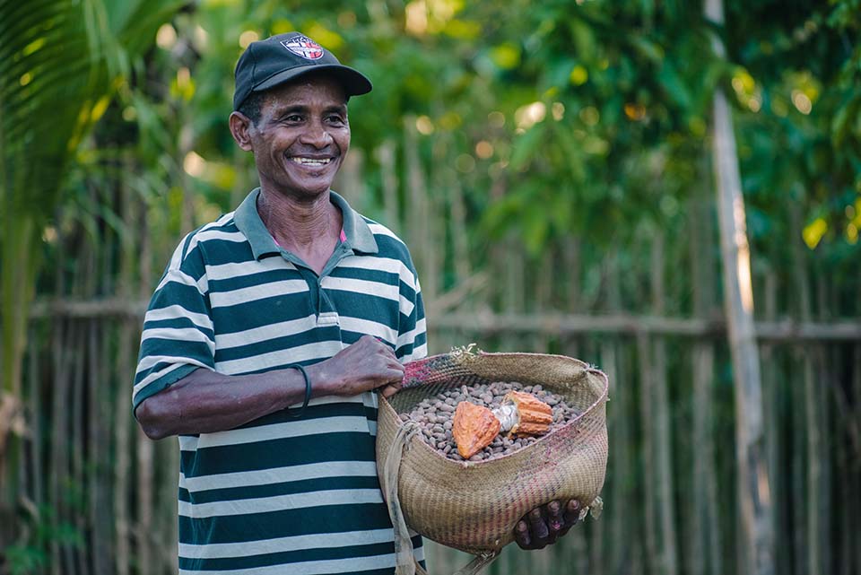 smiling Malagasy man holds basket full of cacao beans