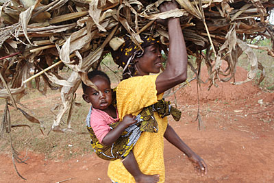 Mary Kamangeni carries her grandson Trust while she gathers dried-up cornstalks to spread in her fields to help retain water and nurture the soil. Photo by Sara A. Fajardo/CRS