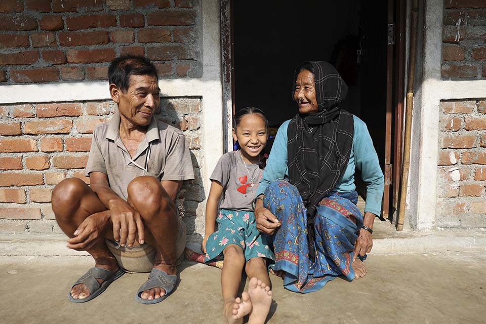 Nepal family sits outside their new home 