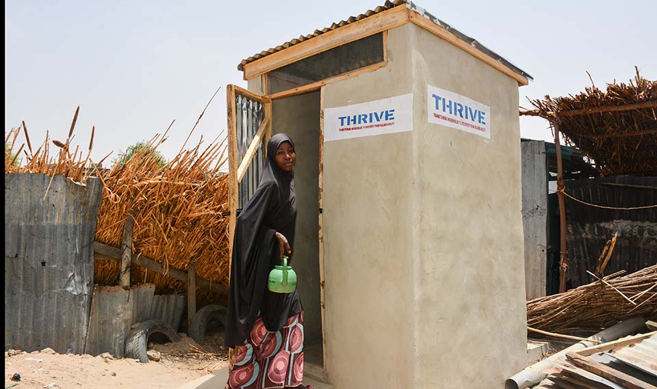 woman stands outside latrine in Nigeria