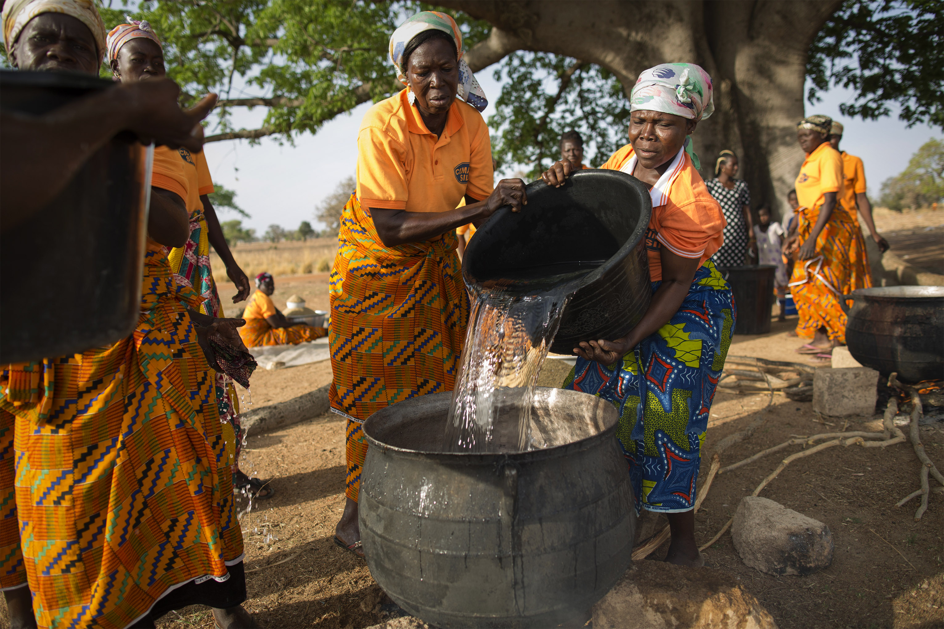 When rising temperatures bring destructive weather patterns and cause crops to wither, the women in Awaradoni village work together as a support system. Here, they are processing and making rice. When rising temperatures bring destructive weather patterns and cause crops to wither, the women in Awaradoni village work together as a support system. Here, they are processing and making rice. Photo by Jake Lyell for CRS