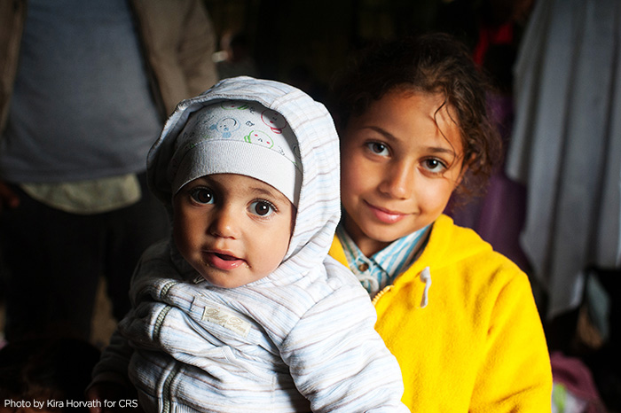 Syrian refugee Obama Basheer, holds her sister, Joud, inside a refugee aid station in the Kanjiza, Serbia. Syrian refugees arrived by double-decker bus from Belgrade, CRS is assisting the Syrian people in transit all through the region.