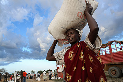 A woman in Makol Cuei, South Sudan, balances a 110-pound bag of sorghum she received as payment for 20 days of road construction. Photo by Sara A. Fajardo/CRS