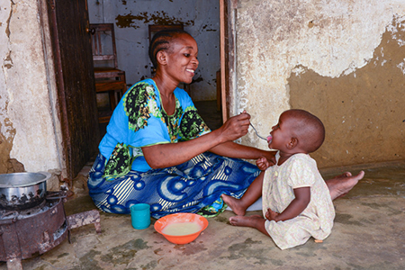 Tatu Omari feeds her daughter Mwanaisha. Tatu and her twin daughters participate in the CRS THRIVE project, which encourages good nutrition and positive parenting. Photo by Philip Laubner/CRS