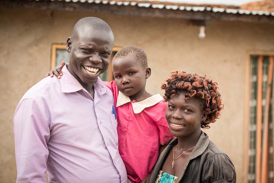 South Sudanese family standing outside their Uganda home