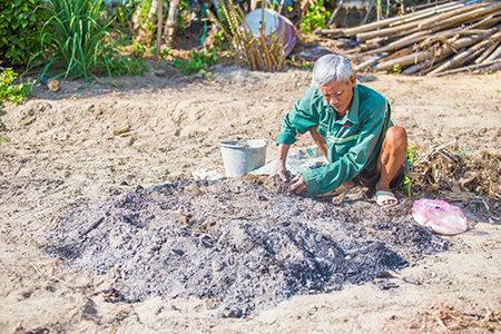 Photo by Lisa Murray for CRS Tue applies a new composting technique, involving the layering of animal dung to bring extra moisture to the soil during increasingly severe dry spells that have hit Quang Nam province in recent years.