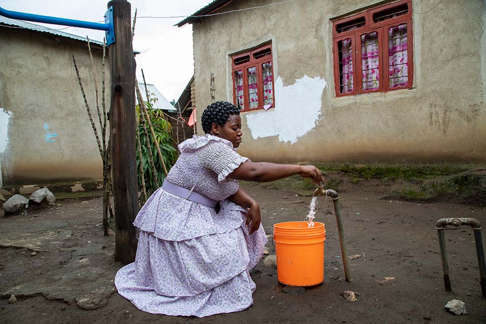 woman fills bucket from water tap in Tanzania
