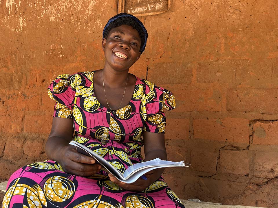 woman practices reading outside her home in the Democratic Republic of the Congo