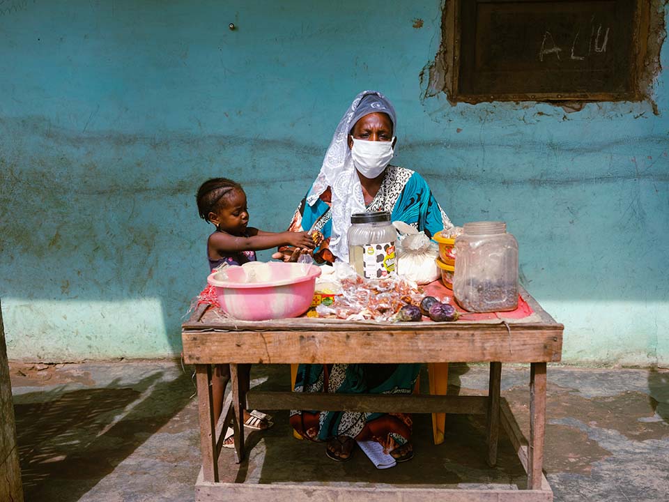 woman seated wearing mask and selling vegetables and spices at a small roadside stall