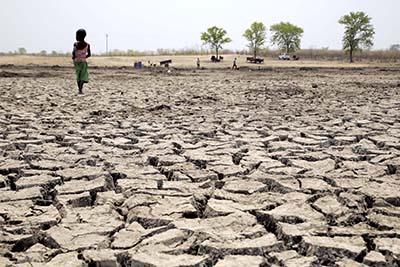 A child walks across a stark landscape, once a watering hole. Now water can only be found by digging deep into the last remaining spots of mud. Still, with water so scarce, people continue to bring their animals here to drink. Photo by Nancy McNally/CRS