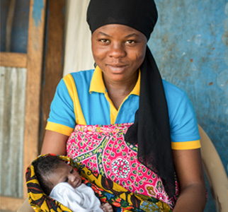 Woman with a head wrap holding a baby, smiling.
