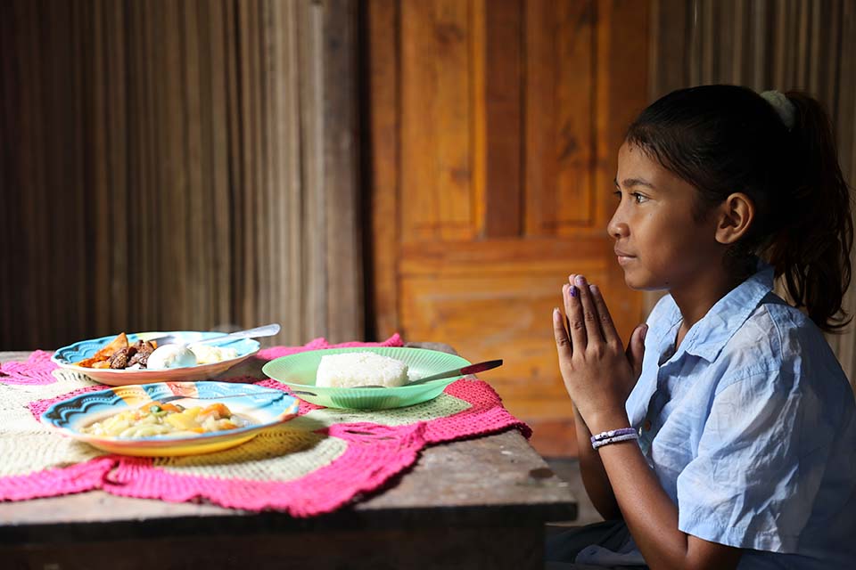 girl prays at dinner table in Timor-Leste