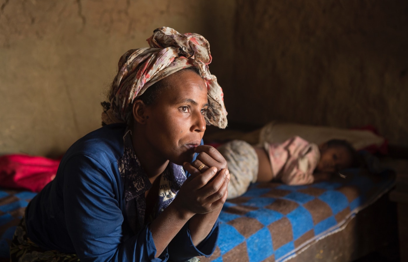 Ganet Gelgehu sitting on her daughter's bed while she lays down.