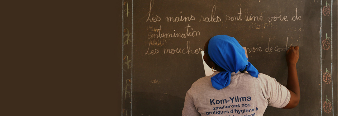 Woman with blue headscarf writing on a chalkboard.