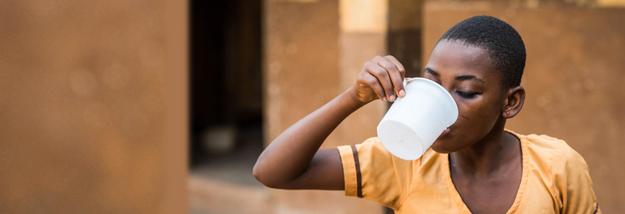 Young girl in yellow drinking from a cup.