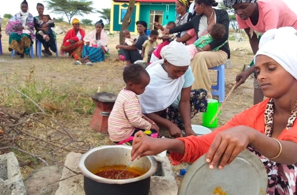 Enthiopian neighbors and families sitting in a circle eating a meal.