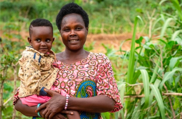 Rwandan mother carrying her child in front of farm