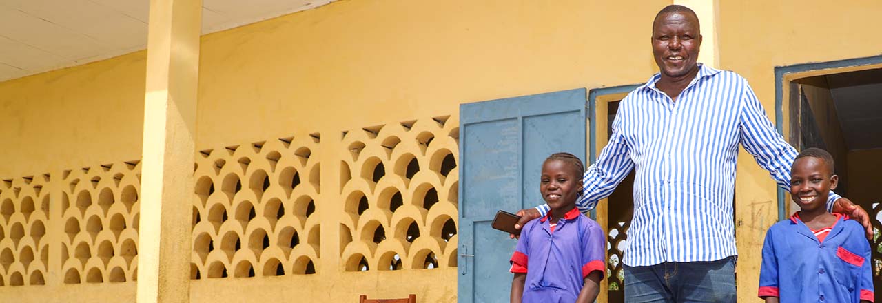 teacher stands with two of his fifth-grade students in Cameroon