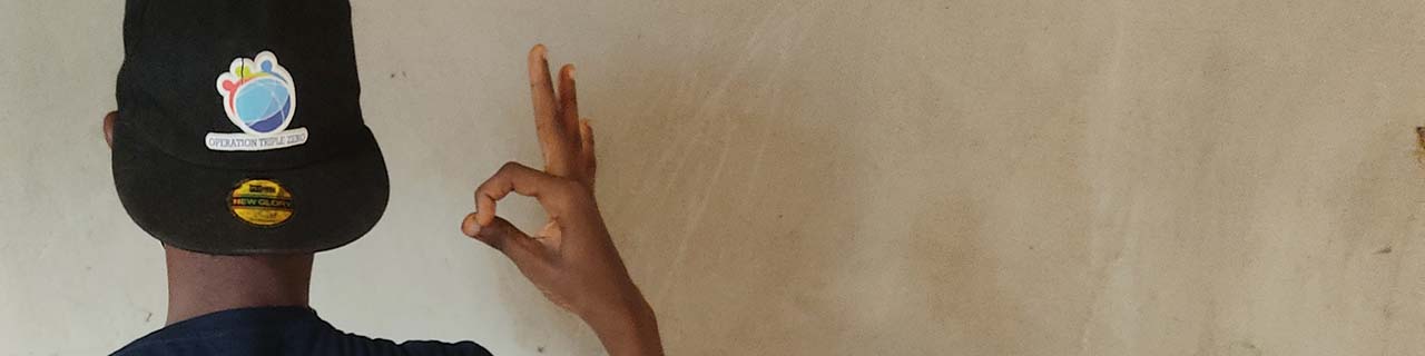 young Nigerian man wearing ball cap and making zero sign with back to camera