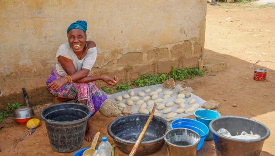 Savings group member sits outside among materials she uses to make shea butter.