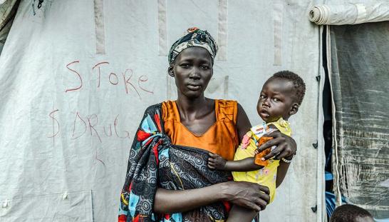 A woman holding a child in front of a tent.