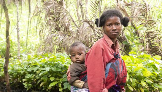 woman with baby on back in front of a garden