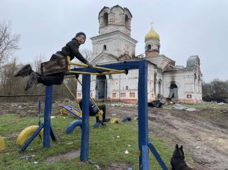 Children play on a playground outside a destroyed building.