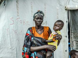 A woman holding a child in front of a tent.