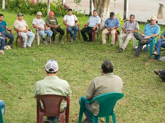 Community members seated in a large circle outdoors, engaged in a group discussion on a grassy area.