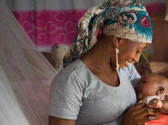 A woman sitting on a bed holding a baby.