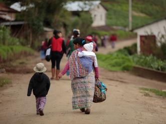 Una mujer caminando con maletas y sus dos hijos. Uno a su lado y el otro a su espalda.