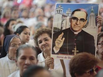 Una señora eleva una imagen de San Oscar Romero entre una multitud.
