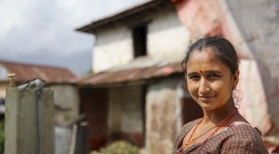 woman stands outside damaged home in Nepal 