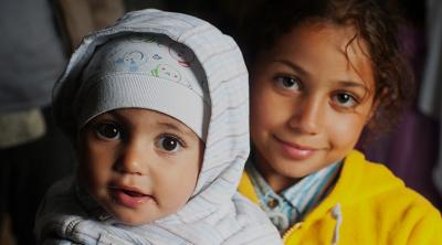 Syrian refugee Obama Basheer, holds her sister, Joud, inside a refugee aid station in the Kanjiza, Serbia. Syrian refugees arrived by double-decker bus from Belgrade, CRS is assisting the Syrian people in transit all through the region.