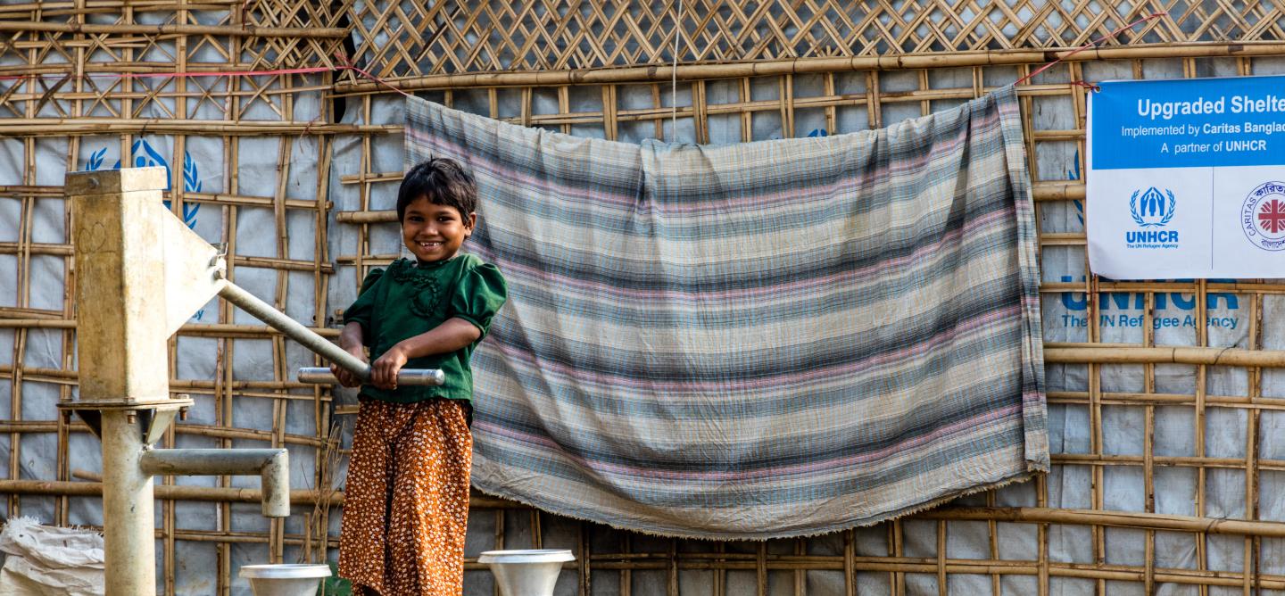 young girl in green shirt pumps water from an outdoor well
