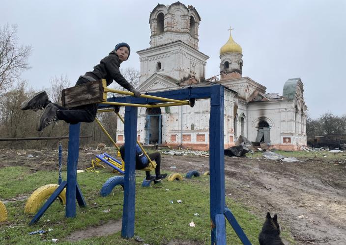 Children play on a playground outside a destroyed building.