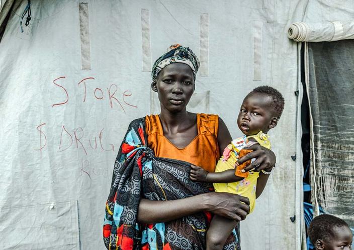 A woman holding a child in front of a tent.