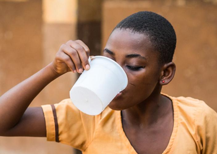 A girl drinking water from a plastic cup.