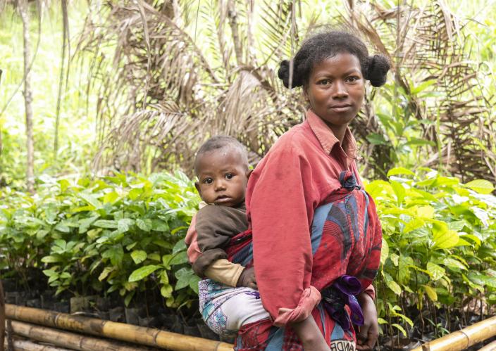 woman with baby on back in front of a garden