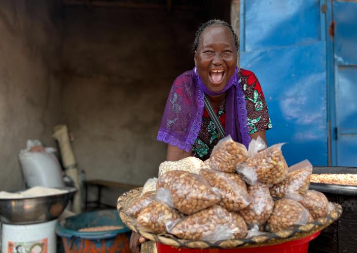 A woman wearing a colorful outfit standing behind a large basket filled with small plastic bags of nuts.
